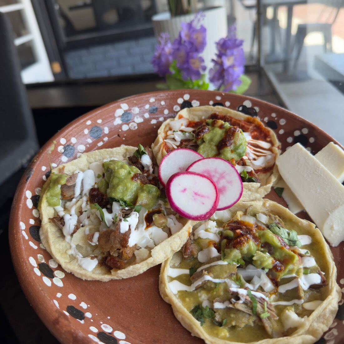 Picaditas on a painted clay plate, topped with salsa, crema, radish and avocado