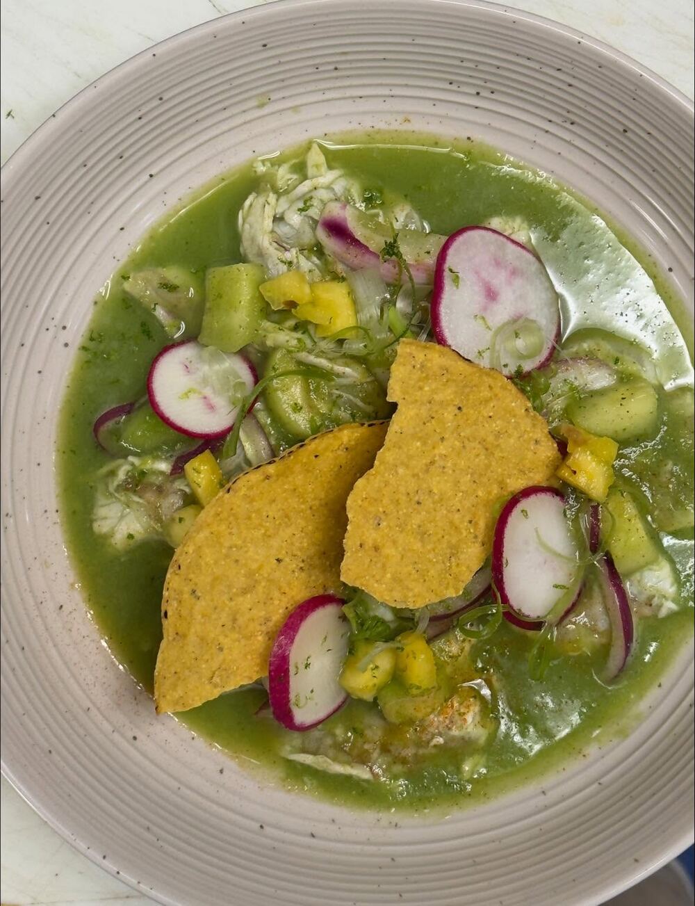 Green pozole with radish, corn and tortilla chips in a shallow bowl