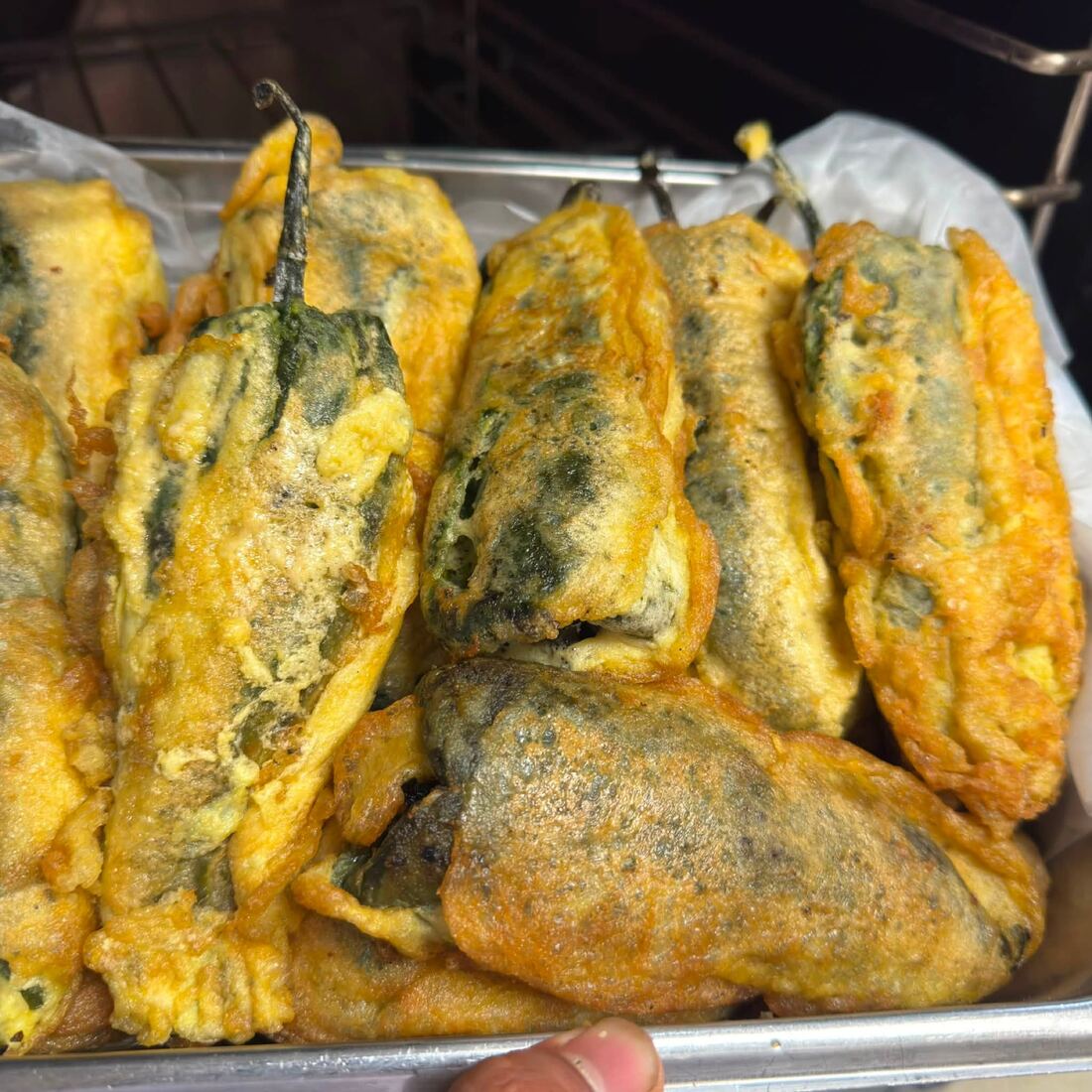 A tray of battered poblano peppers stuffed with Oaxaca cheese, fresh out of the pan